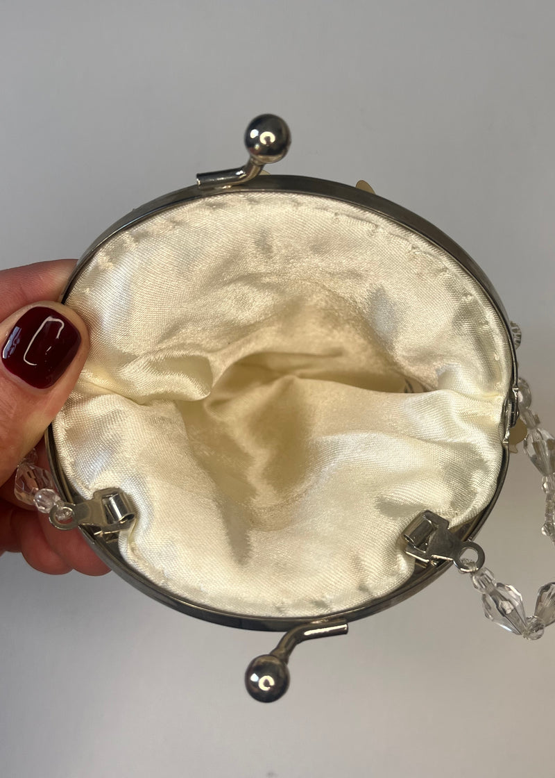 Hand holding a round metallic clutch with a satin interior against a neutral background