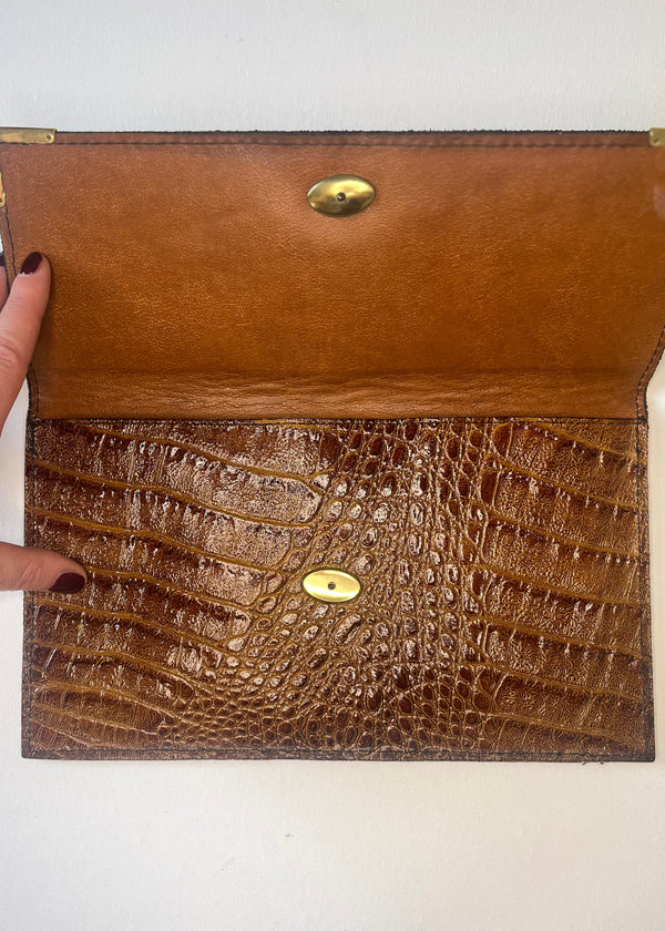 Brown leather clutch with crocodile texture and gold accents on a white background