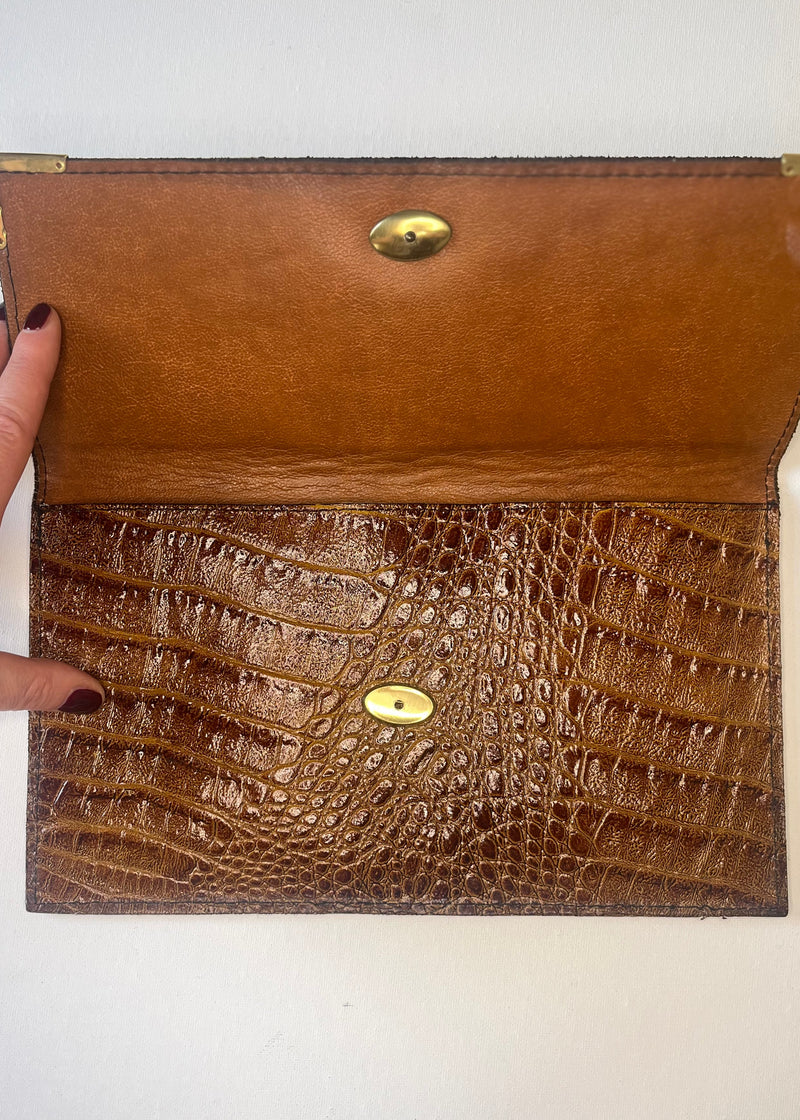 Brown leather clutch with crocodile texture and gold accents on a white background